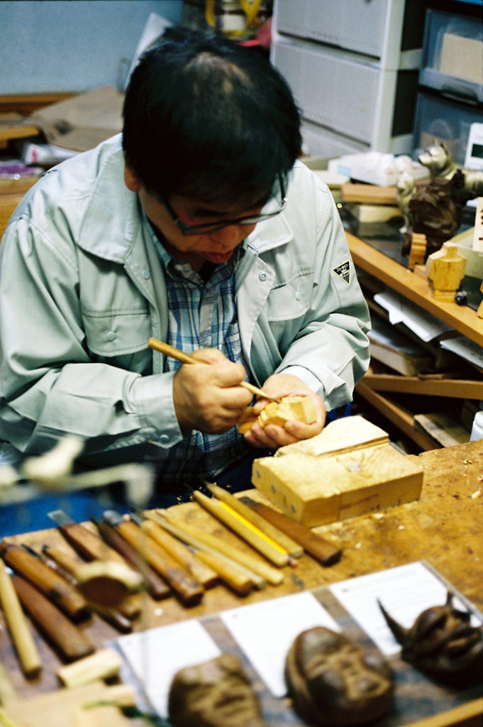 Employed craftsmen sit in deep concentration as they whittle and carve traditional Japanese artifacts. 