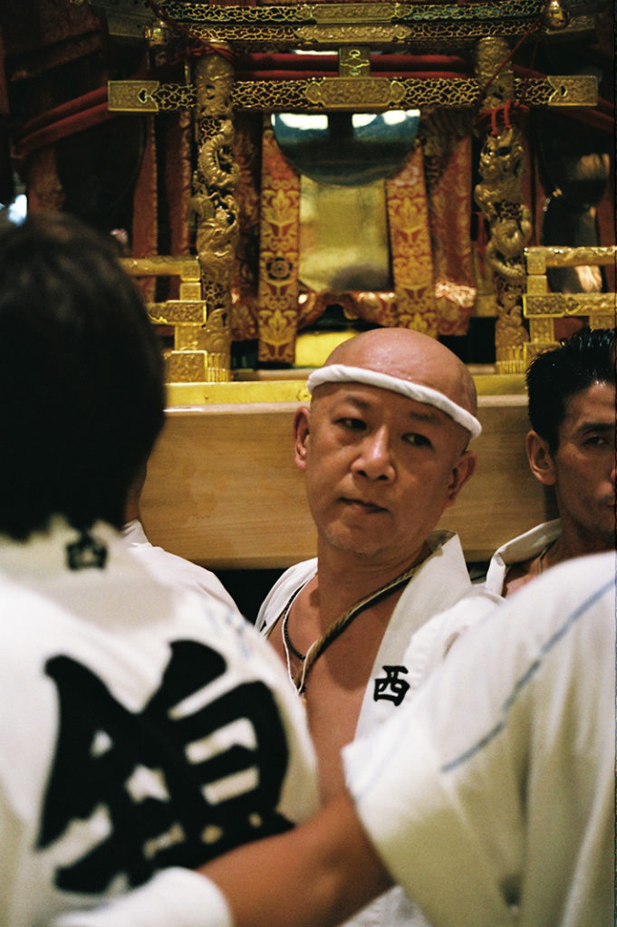 Swarms of men bear the shoulder-bruising burden of bearing the Mikoshi through Kyoto's endless maze of side-streets.