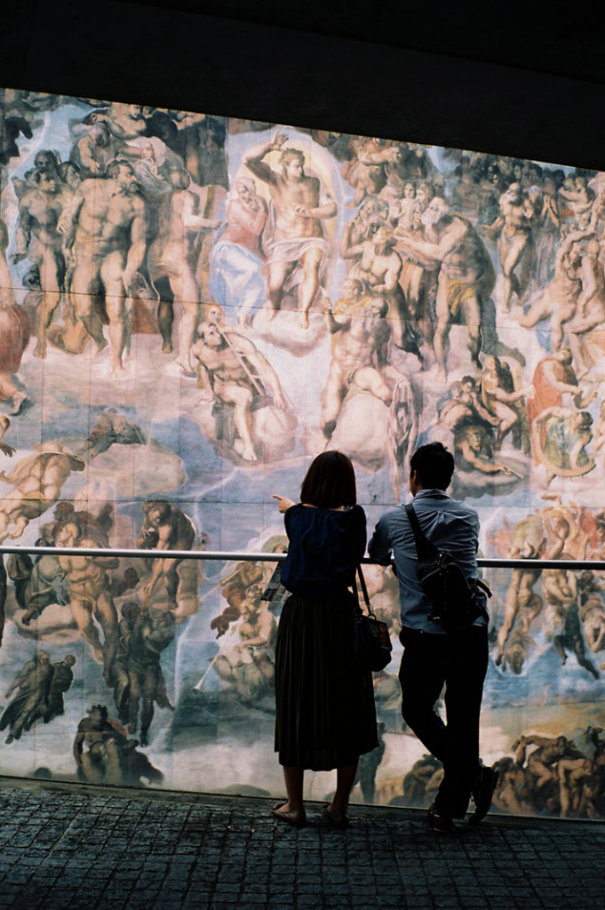 A couple stand on a balcony overlooking the towering "Last Judgement" by Michelangelo. Tags: architecture, design, Tadao Ando.