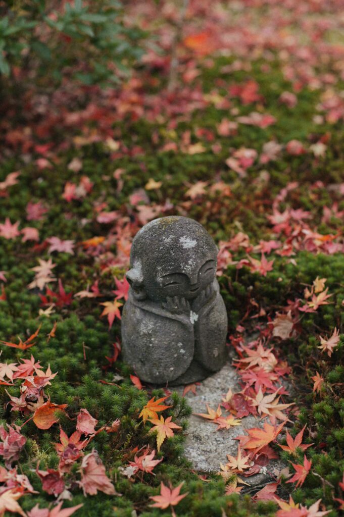 A cheerful little Jizo Bosatsu enjoys the autumn colours at the temple.