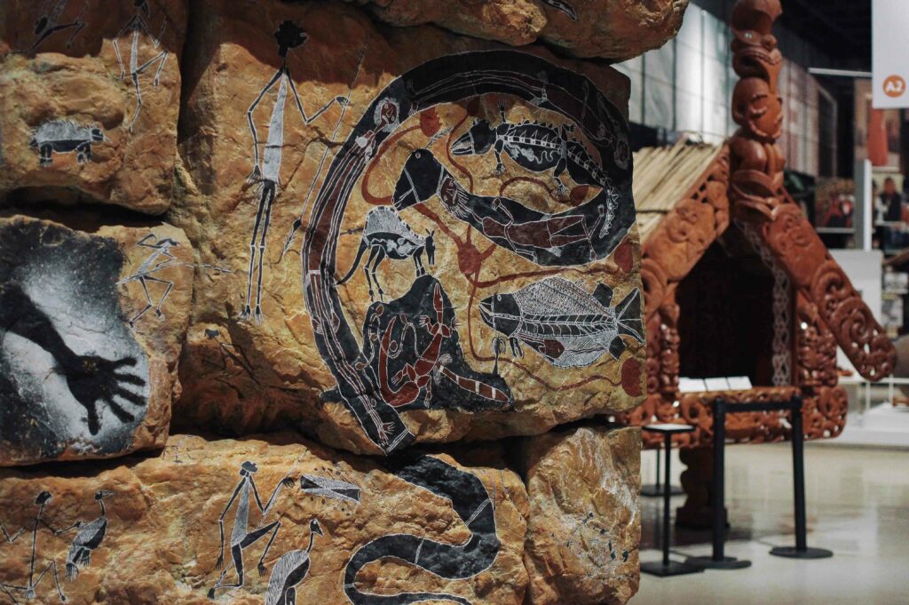 Aboriginal Australian artwork displays sit in front of a Māori pataka from Aotearoa / New Zealand.
